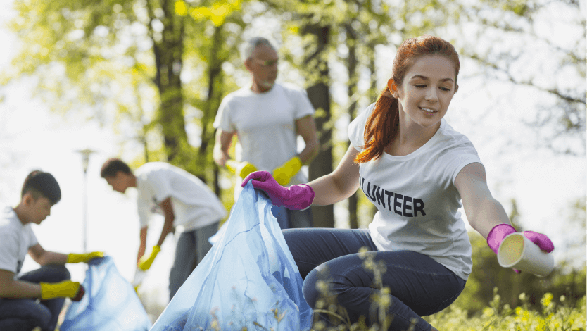 Group of volunteers cleaning up their park. Red haired woman wearing purple gloves kneeling in the foreground.
